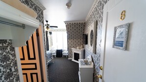 A hotel room with patterned wallpaper, a white door with a gold number, a small white table, a mirror, and a framed picture on the wall. - The Maple Inn B&B (Parrsboro)