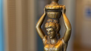 A close-up of a golden statue with a vase on its head.