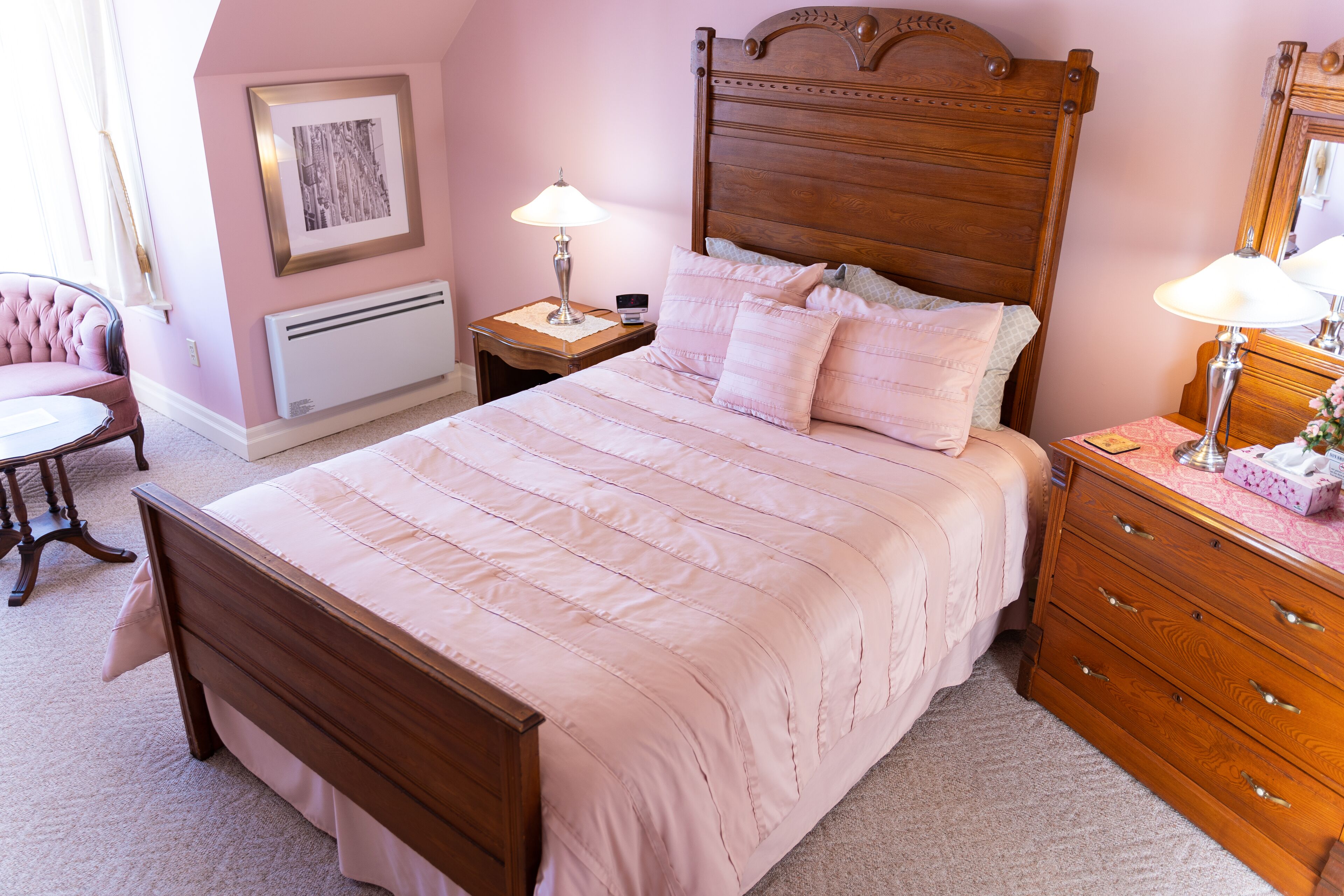 A bedroom with a wooden bed, a nightstand with a lamp, a dresser, and a chair.