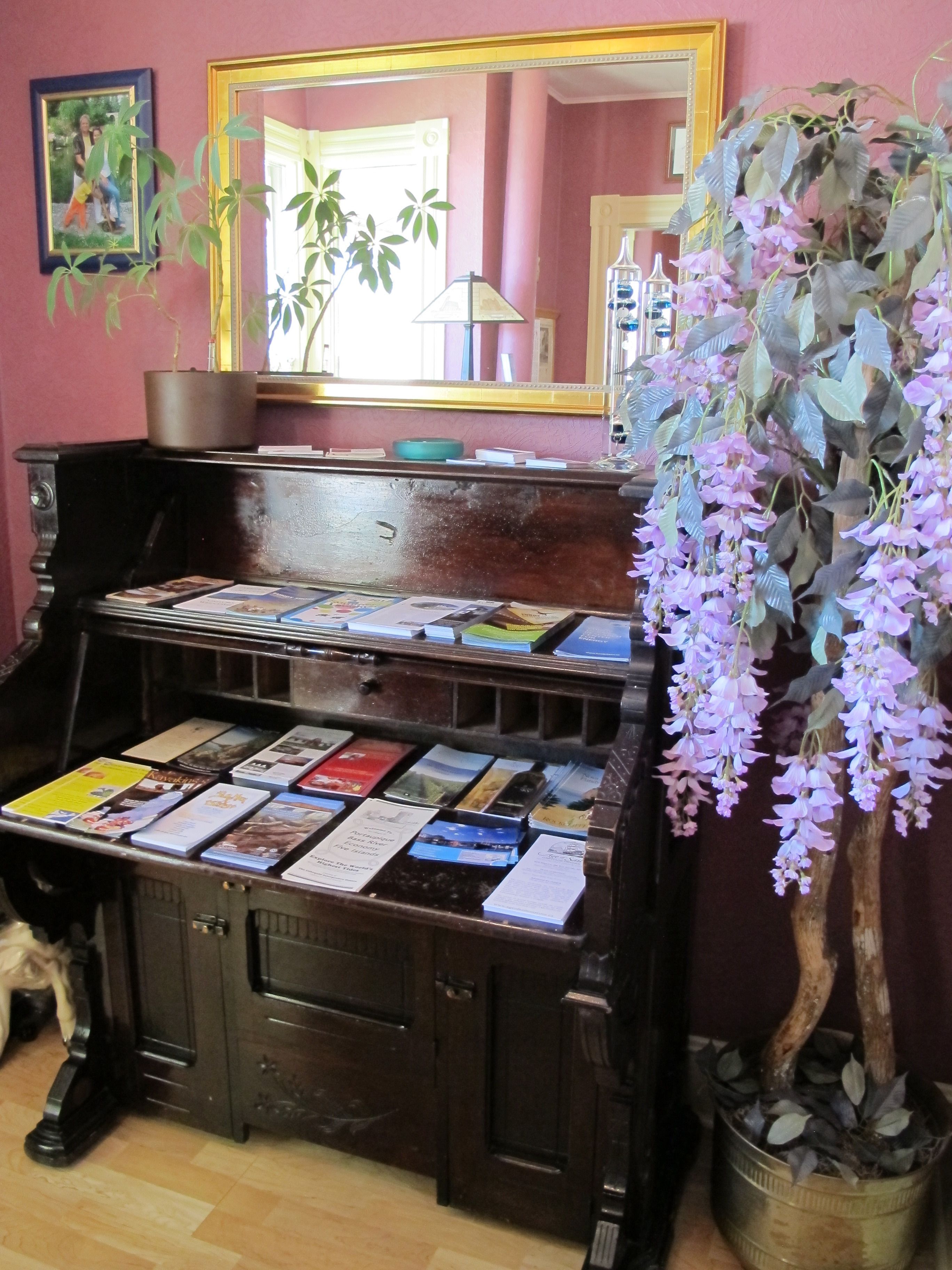 Een kamer met een piano, boeken, een spiegel en een hangplant.