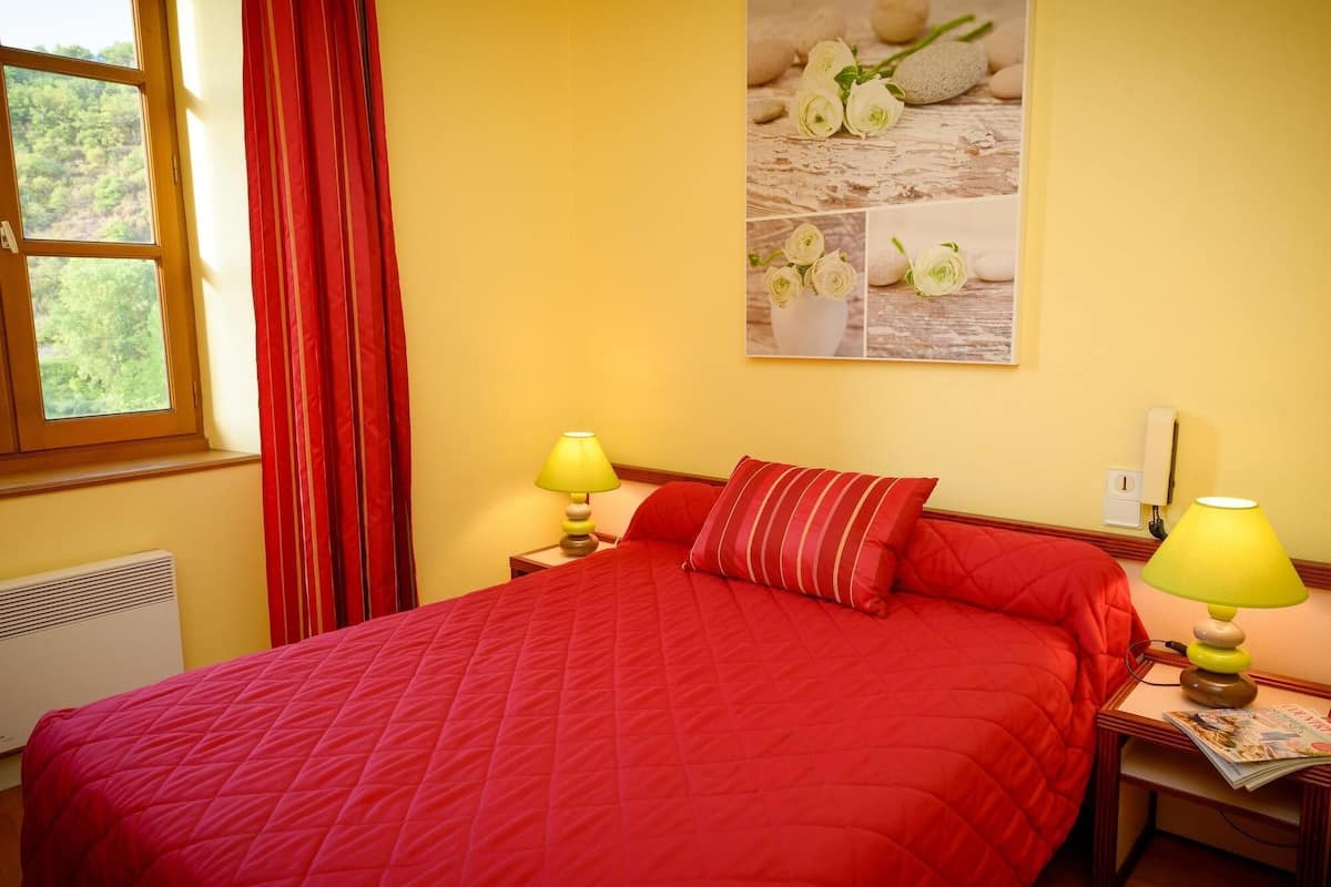 A room with a bed, two bedside lamps, a window with curtains, and a wall-mounted picture.