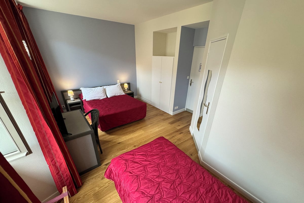 A bedroom with two beds, a desk, and a chair. There is a wardrobe and a door in the room.