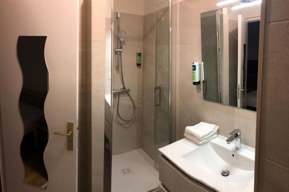 A modern bathroom with a glass shower enclosure, a white sink, and a large mirror.