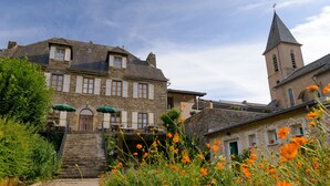 A historic stone building with a tower, a covered staircase, and a flower-filled garden. - Hostellerie des Lauriers (Curvalle)