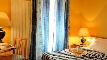 Una habitación de hotel con cama, una silla, un escritorio y una lámpara.