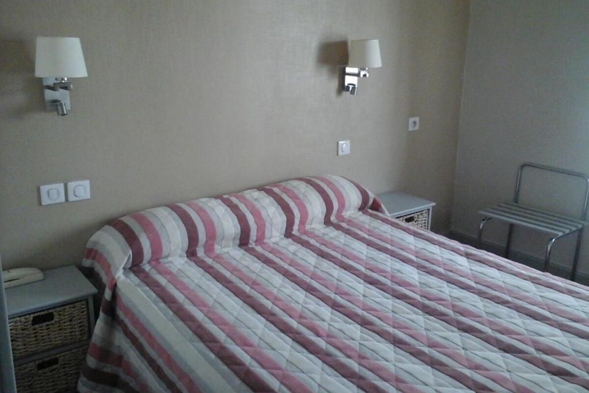 A hotel room with a bed, two bedside lamps, a small bedside table, and a wall-mounted towel rack.