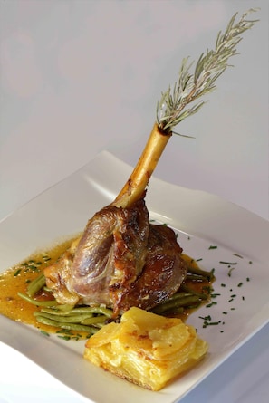 Un plato con un jarrete de cordero, judías verdes y guarnición de patatas.