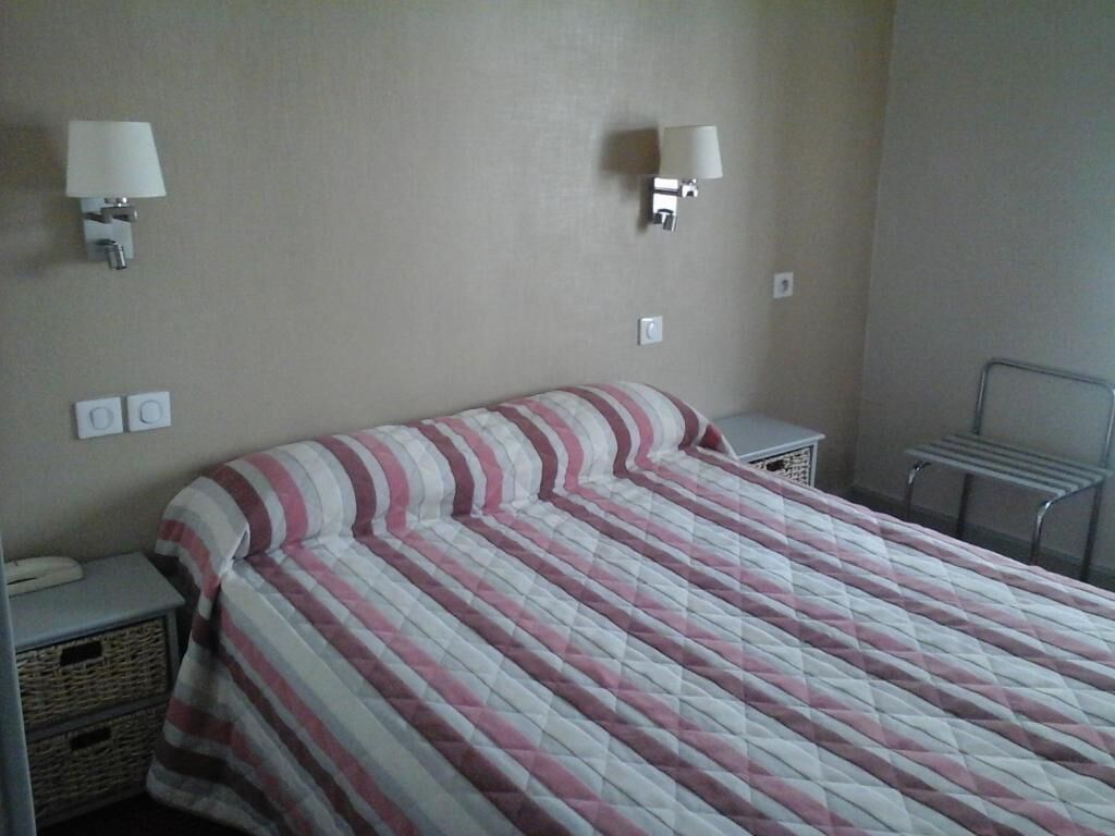 Une chambre d’hôtel comprenant un lit, deux lampes de chevet, une petite table de chevet et un porte-serviettes fixé au mur.