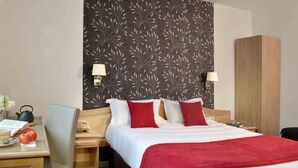 A hotel room with a bed, two bedside tables, a desk, a chair, a wardrobe, and a wall with a leaf pattern. - Le Continental (Chateauroux)