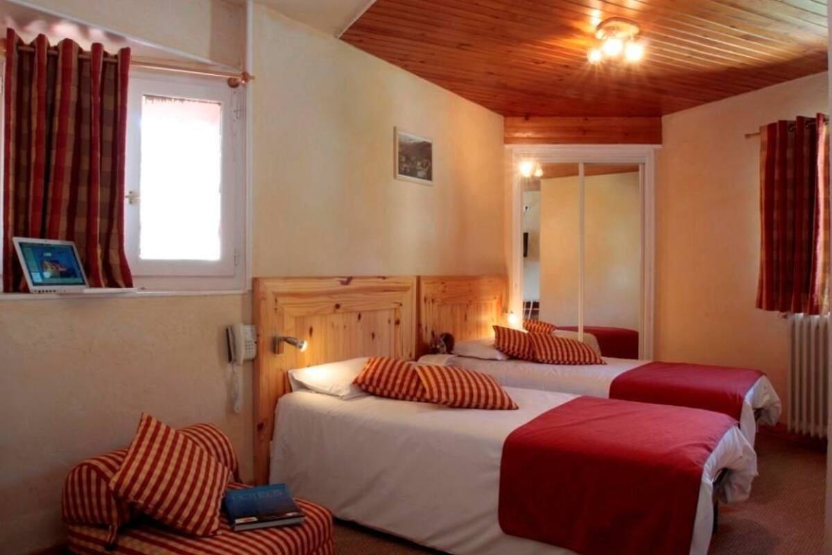 A room with two beds, each with red and white bedding, a wooden headboard, and a small bedside table with a lamp.