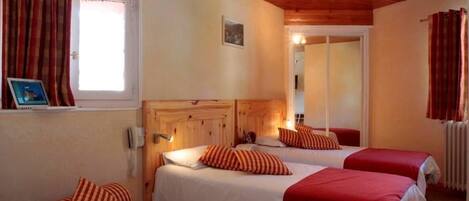 Una habitación con dos camas, cada una con ropa de cama roja y blanca, un cabecero de madera y una mesita de noche pequeña con una lámpara.
