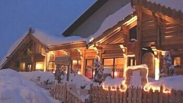 Una cabaña de madera con entrada cubierta de nieve y luces exteriores iluminadas.