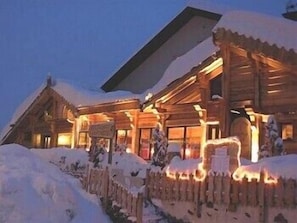 A wooden lodge with a snow-covered entrance and illuminated exterior lights. - L'Ecureuil (Saint-Etienne-de-Tinee)