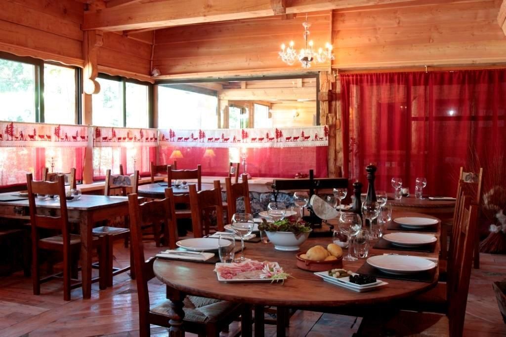 A wooden dining area with tables set for a meal, including plates, glasses, and a bowl of salad.
