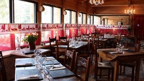Un restaurante con paredes de madera, mesas dispuestas con copas de vino y cubiertos, y un muro con estampado rojo y blanco.