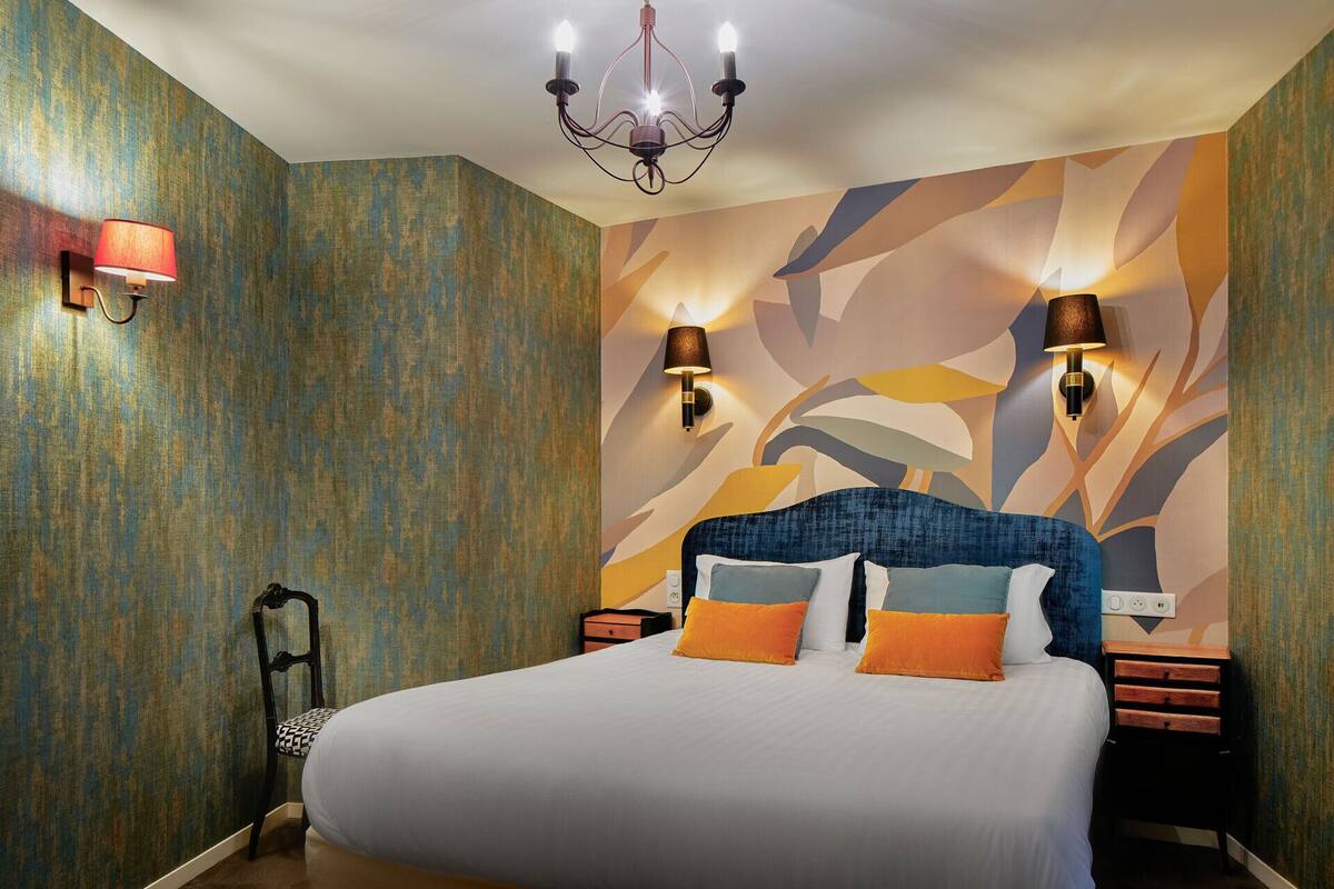 Une chambre d’hôtel avec un grand lit, deux tables de chevet, un lustre et des lampes fixées au mur.