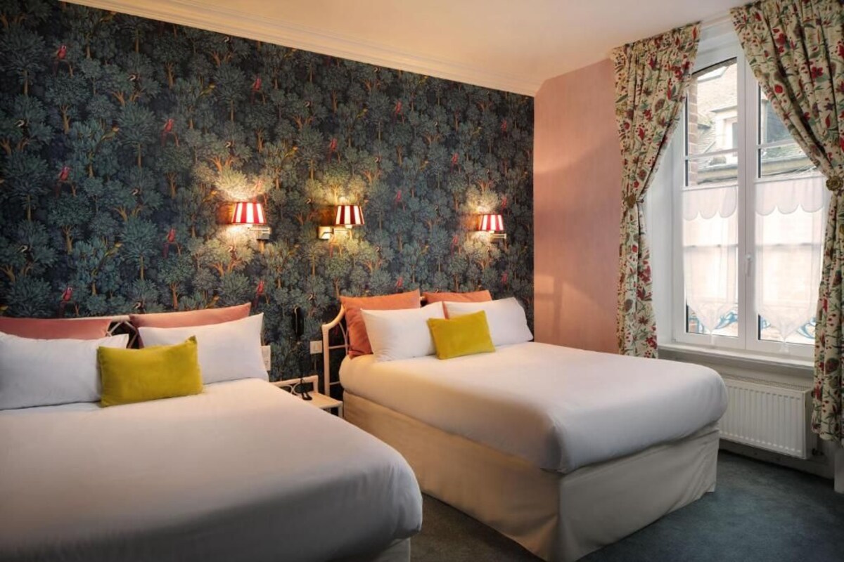 A hotel room with two beds, a floral wallpaper, and a window with curtains.