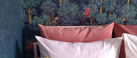 A bed with pillows in white, yellow, and red, against a wall with a jungle-themed wallpaper.