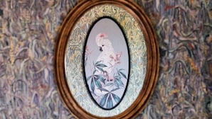 Une œuvre d’art encadrée, ornée de motifs floraux, est accrochée à un mur texturé.