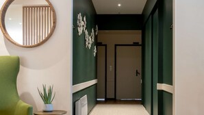 Un interior moderno con una pared de acento verde, un espejo redondo, un sillón verde, una mesita con una planta y una lámpara de techo con diseño.