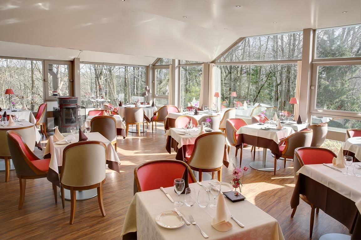 En restaurang med många bord och stolar, stora fönster med utsikt över träd och en öppen spis.