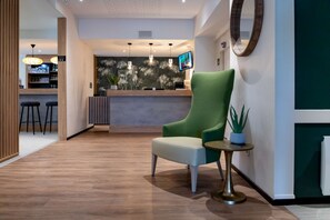A modern reception area with a green armchair, a small side table, and a bar area in the background. - Best Western Auray Le Loch (Auray)