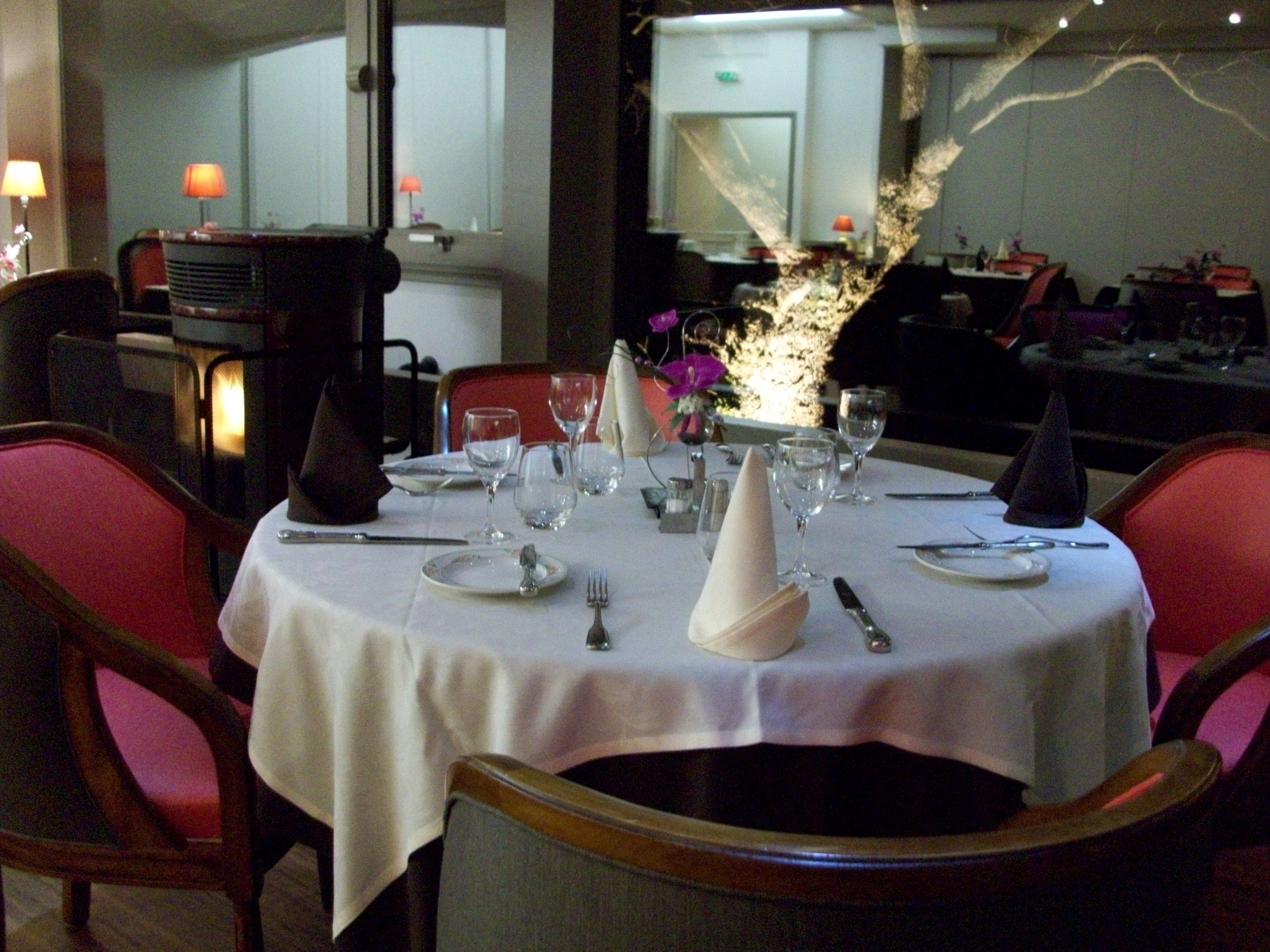 Mesa de comedor dispuesta para cuatro personas, con manteles blancos, cubiertos y vasos de vidrio transparente.