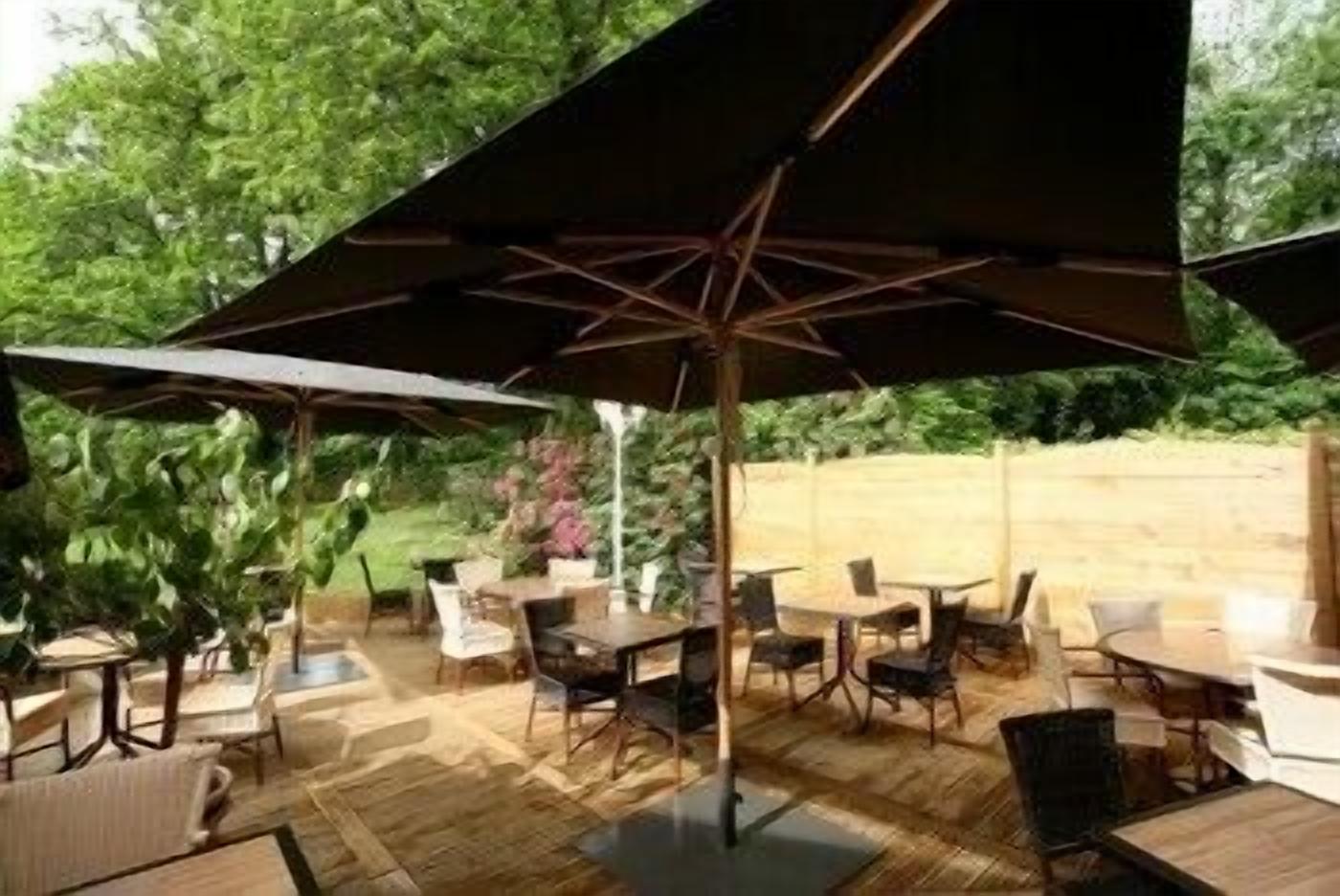 An outdoor patio with wooden tables and chairs, umbrellas, and a wooden deck.