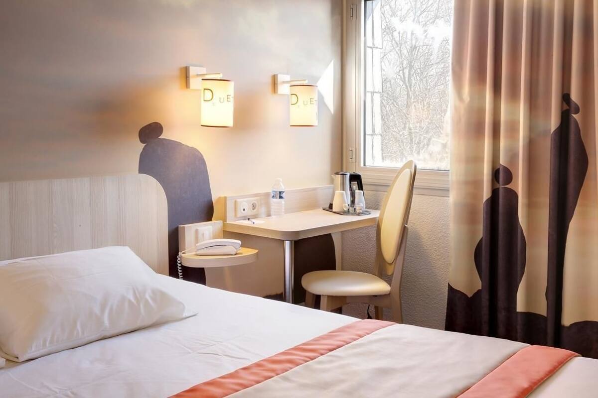 Habitación de hotel con cama, escritorio, silla y ventana con cortinas.