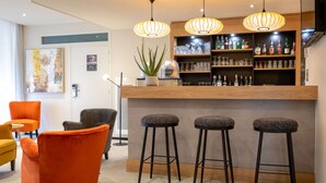 Una zona de bar con taburetes, una estantería con botellas y una planta en maceta.