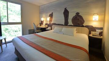 Een hotelkamer met een groot bed, een bureau, een stoel en een televisie aan de muur.