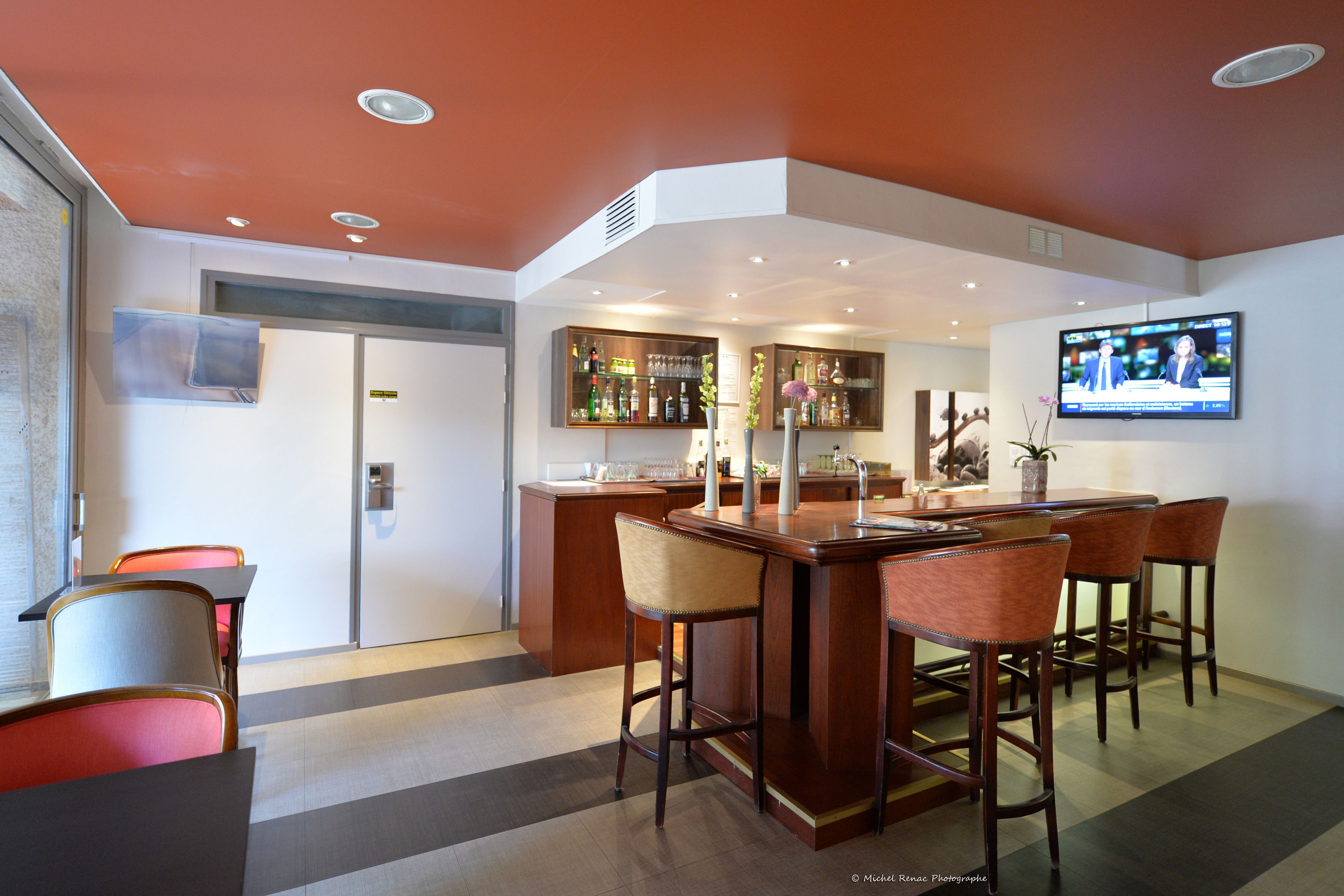 Un área de bar moderna con una barra de madera, taburetes y un televisor montado en la pared.