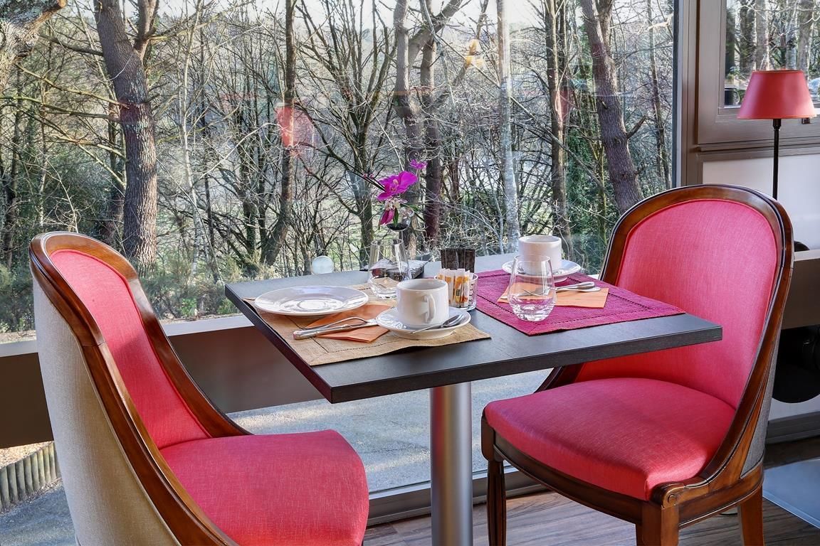 A dining table with two red chairs, a glass of water, a cup, and a vase with a purple flower.
