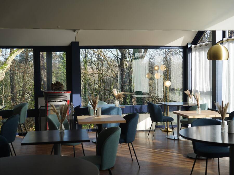 Ein modernes Restaurant mit Blick auf Bäume durch große Fenster. Tische und Stühle sind zum Essen bereitgestellt.