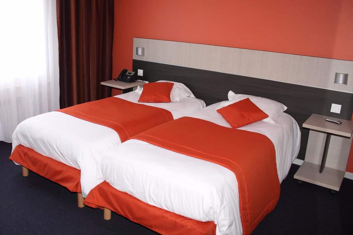 A hotel room with two beds, each with white and orange bedding, a bedside table with a phone, and a nightstand with a remote control.