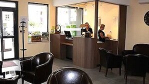 Un hall de hotel con un mostrador de recepción, sillas de cuero negro y un reloj grande en la pared.
