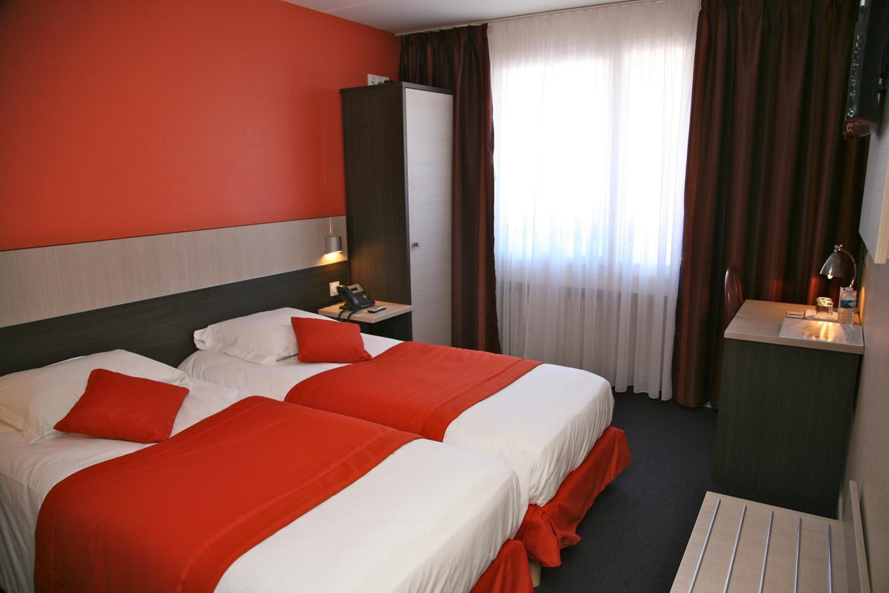 Habitación de hotel con dos camas, un escritorio, un espejo y una ventana con cortinas.