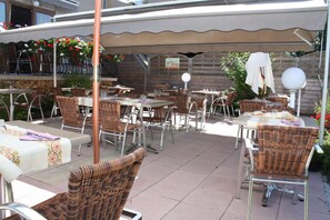 An outdoor patio area with wicker furniture, tables, and chairs under a canopy.