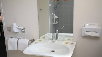 A bathroom with a white sink, a mirror, a towel rack, a hairdryer, and a shower area.