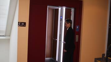 A man standing in a hotel elevator with a red door and a digital display.