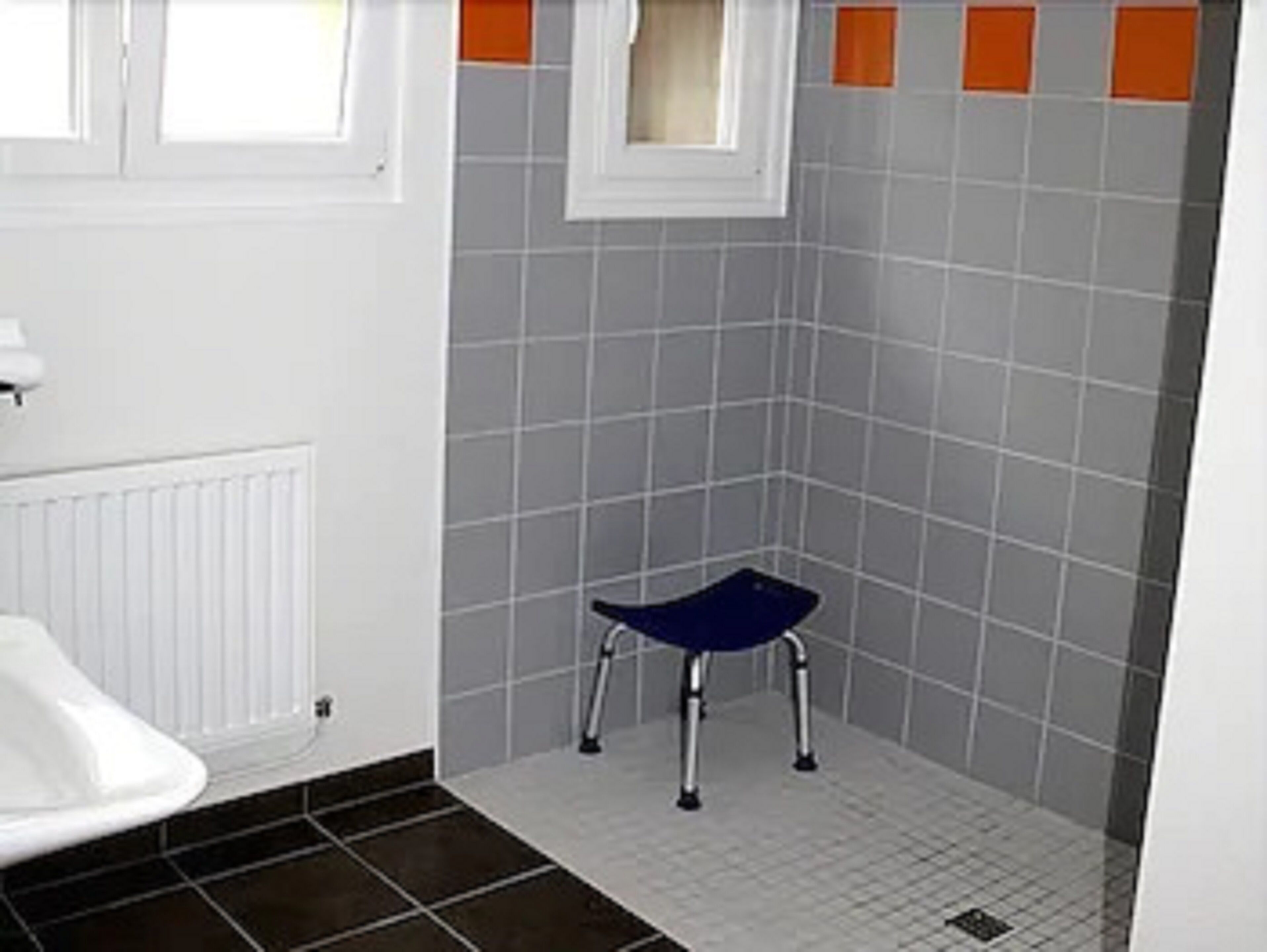 Une salle de bain avec des toilettes blanches, une chaise bleue et des murs carrelés.