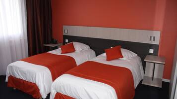 Ein Hotelzimmer mit zwei Betten, jeweils mit weißer und roter Bettwäsche, einem Holzkopfstück und einem kleinen Nachttisch mit Lampe.