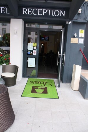 The entrance to a hotel reception with a green mat and a sign above the door.