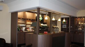 Una zona de bar con mostrador, estantes llenos de copas y botellas, y lámparas colgantes.