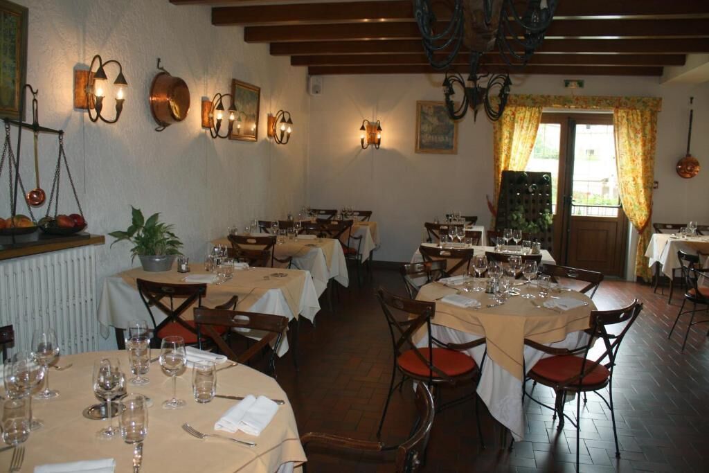 A restaurant with multiple round tables set for dining, featuring white tablecloths and wooden chairs.