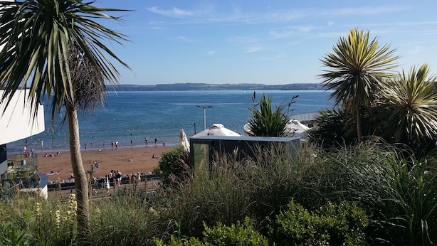 A beach with people, palm trees, and a view of the sea. - The Baytree (Torquay)