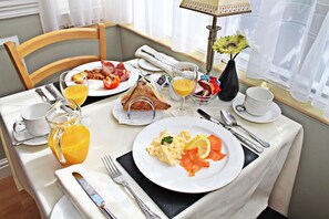 A breakfast setting with a table set for two, including plates of eggs, bacon, toast, and a glass of orange juice. - The Baytree (Torquay)