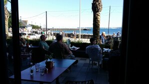 An outdoor seating area with tables and chairs, overlooking a busy waterfront with people and boats. - The Baytree (Torquay)