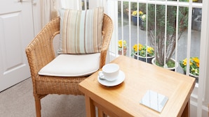 A wicker chair with a cushion and a white cup on a wooden table. - The Baytree (Torquay)