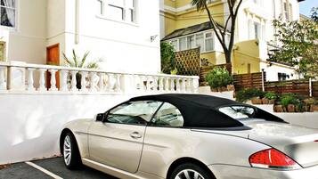 A white convertible car parked in front of a building with a white fence and a balcony.